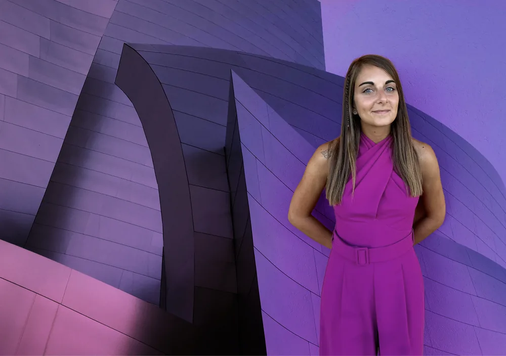 Francesca Buono, fondatrice di FMB Design, in abito magenta davanti a una parete viola