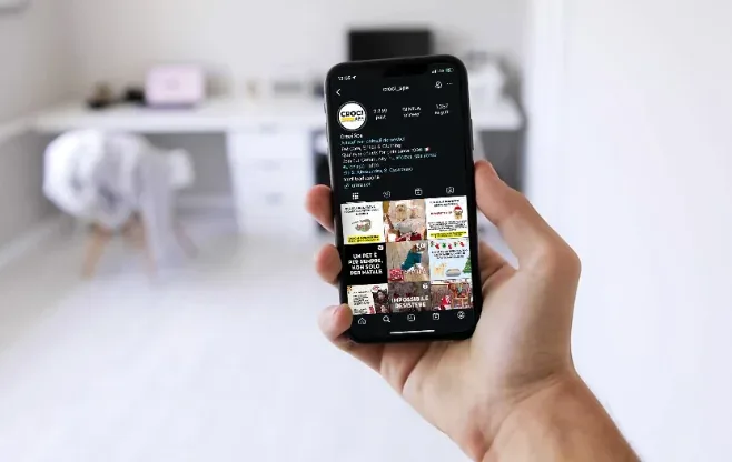 Mano che tiene uno smartphone con il feed social di Croci Group